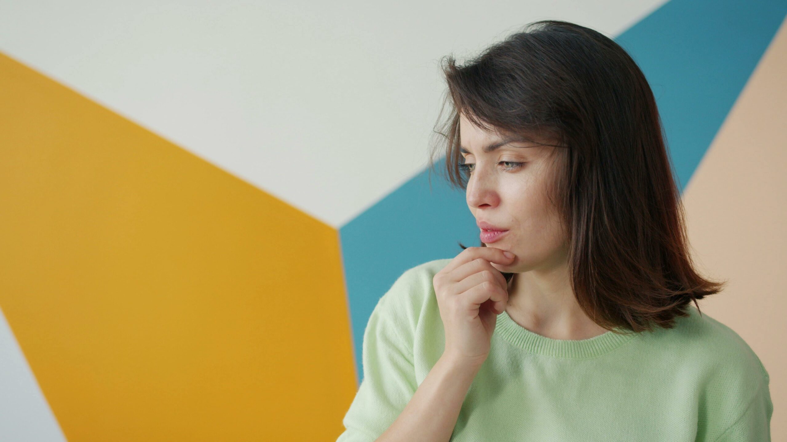 Young woman in contemplation against a colorful geometric background, indoors.